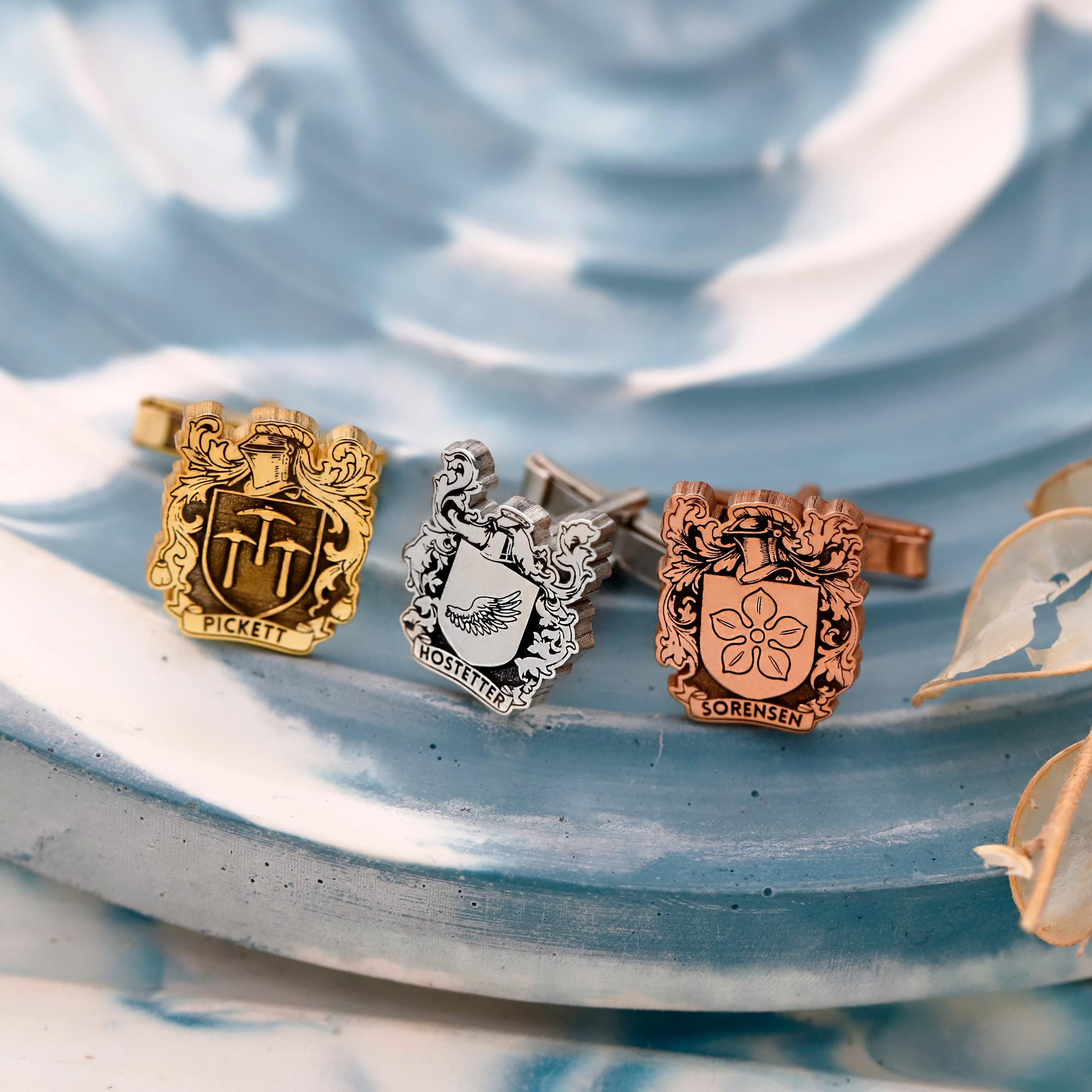 Three cufflinks with engraved designs on a textured blue surface