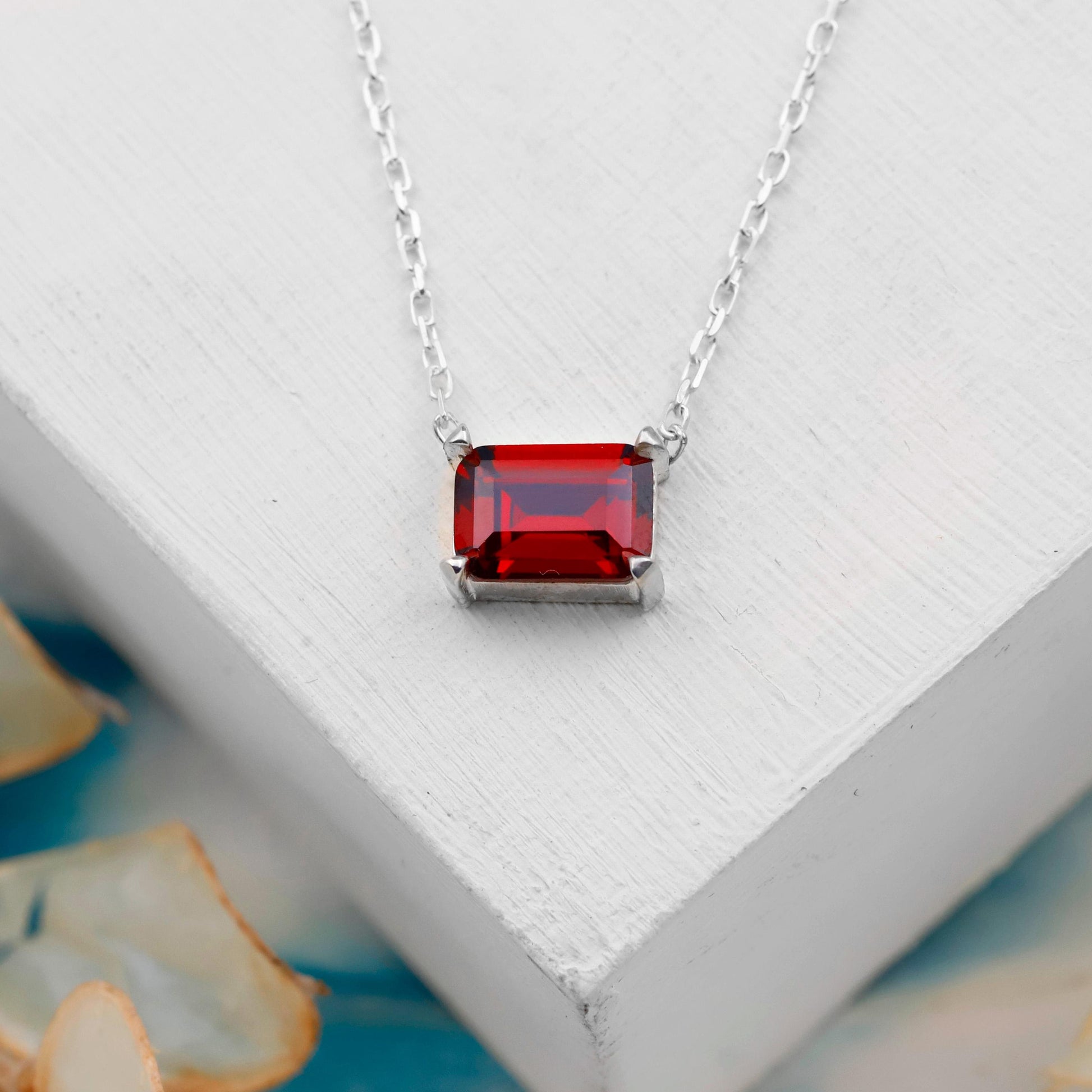 Silver necklace with a red gemstone pendant on a white surface