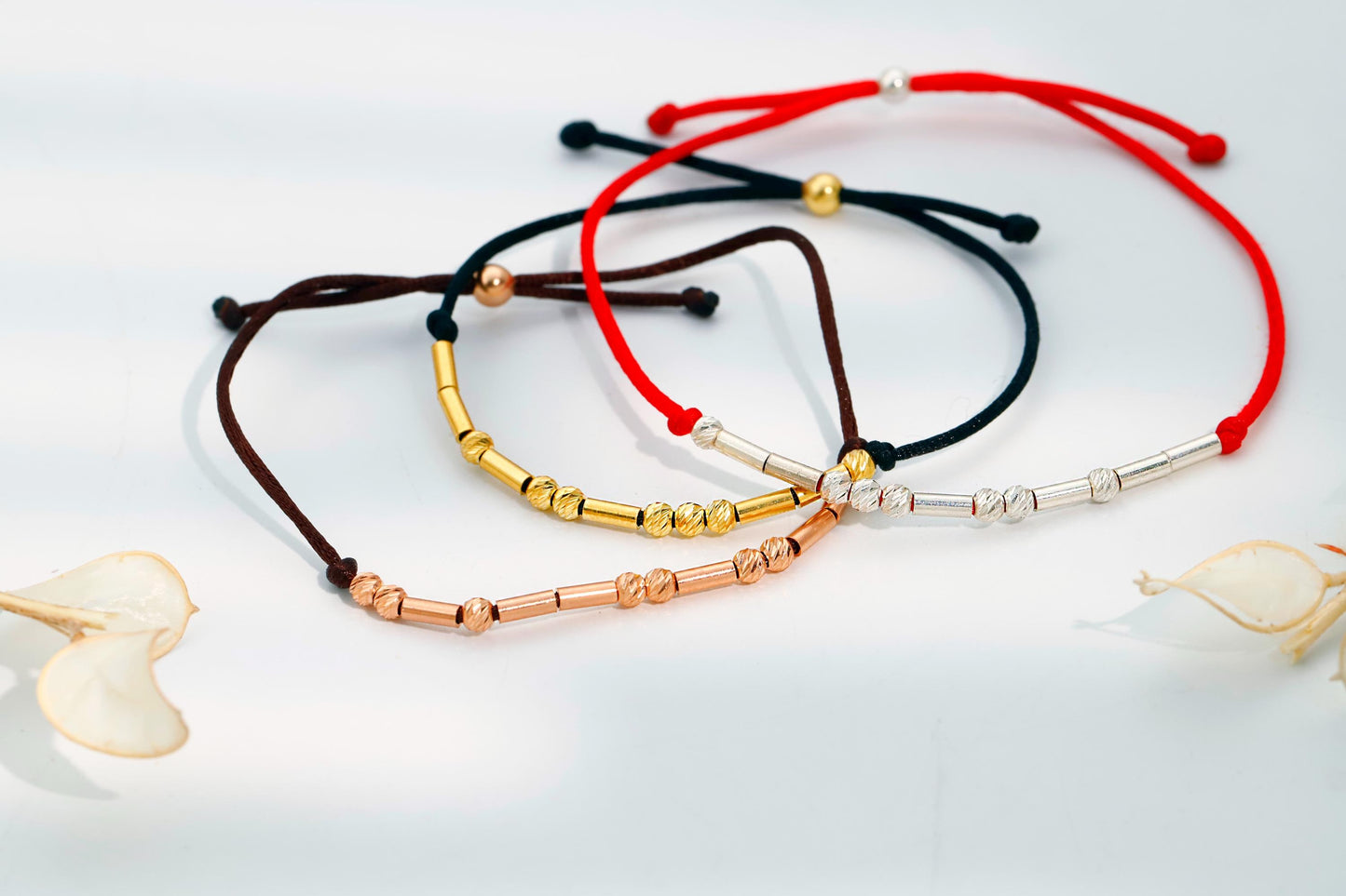 Set of four beaded bracelets in red, black, gold, and silver on a light background.