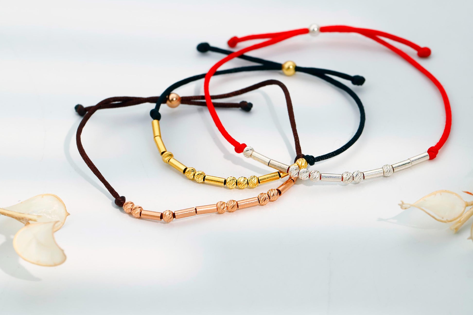 Set of four beaded bracelets in red, black, gold, and silver on a light background.