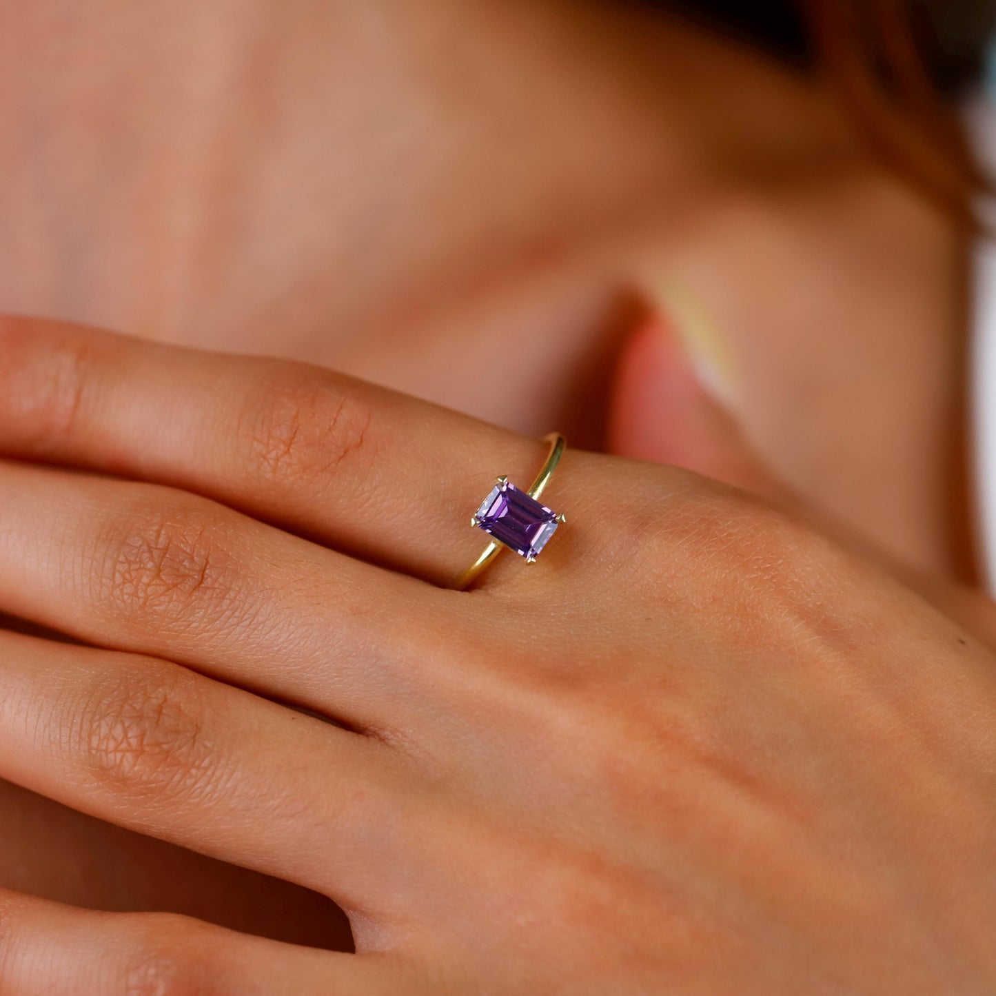 Gold ring with a purple gemstone on a person's finger