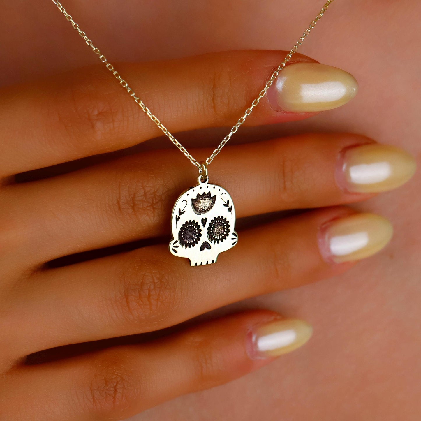 Gold skull necklace on a hand with beige nail polish