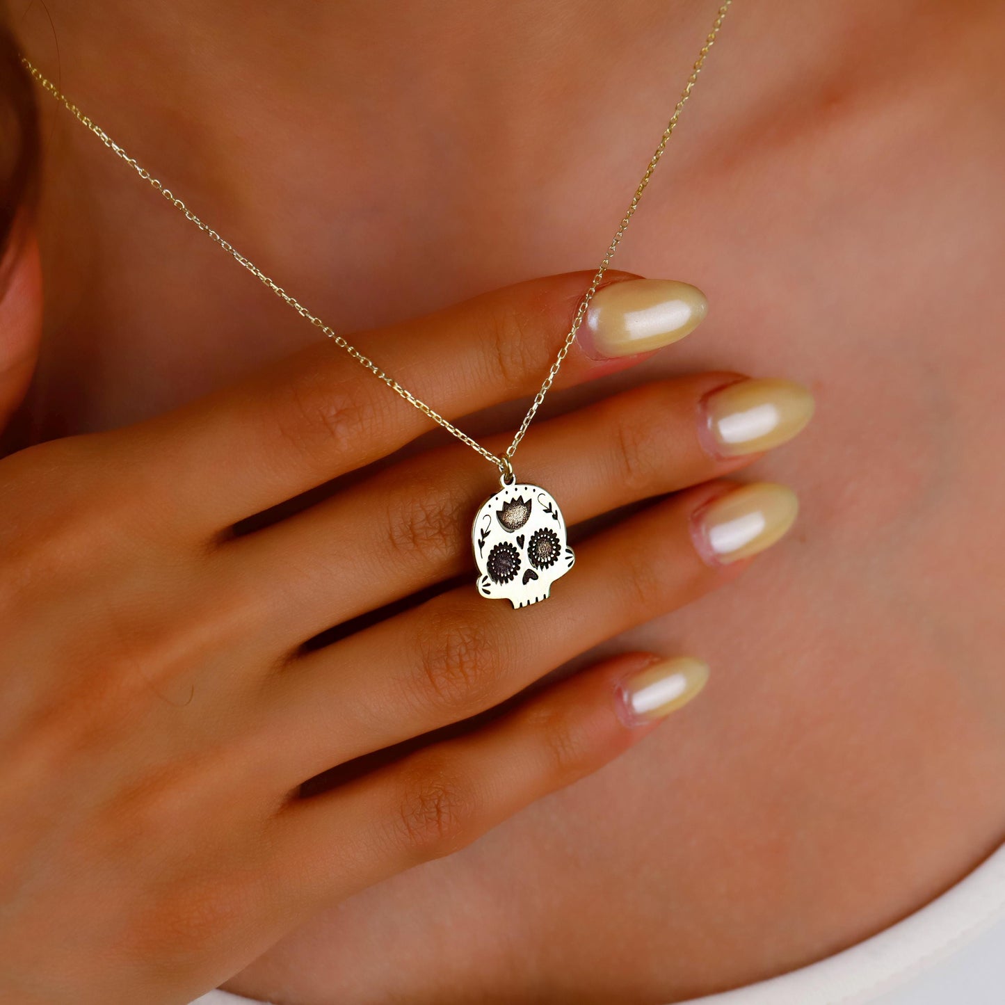 Gold necklace with a skull pendant held by a hand against a neutral background