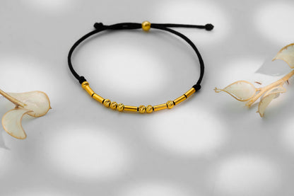 Gold bracelet on a black cord with a soft white background