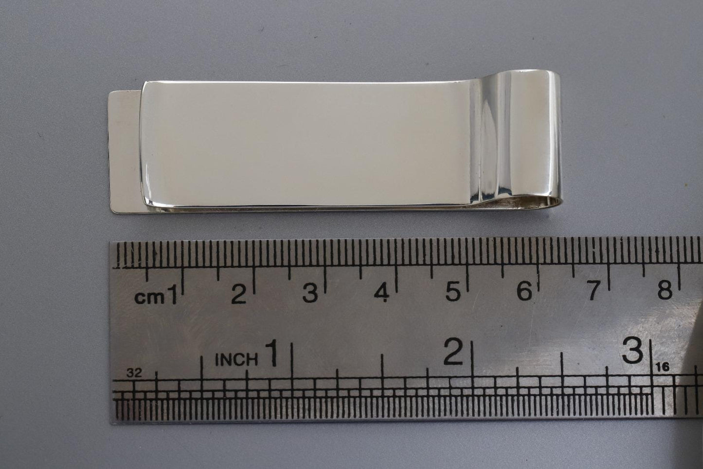 Silver money clip next to a ruler on a gray background