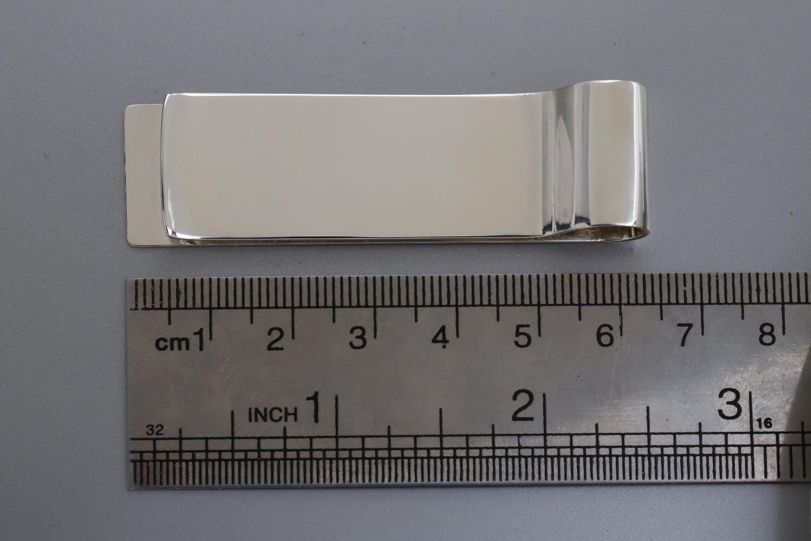 Silver money clip next to a ruler on a gray background
