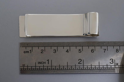 Silver money clip next to a ruler on a gray background