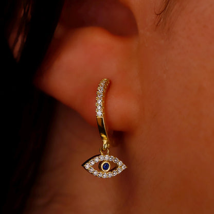 Gold hoop earring with an eye design worn on an ear.