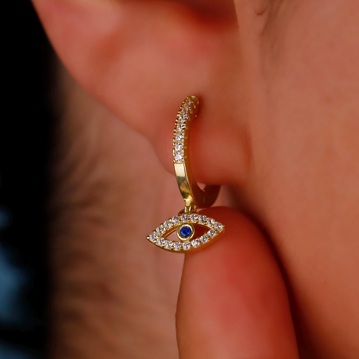Gold earring with a blue gemstone and clear stones worn on an ear.