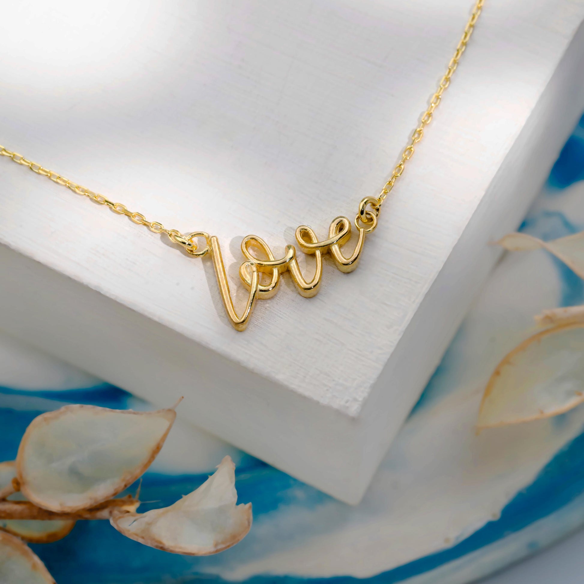 Gold necklace with 'love' pendant on a white surface with floral elements.
