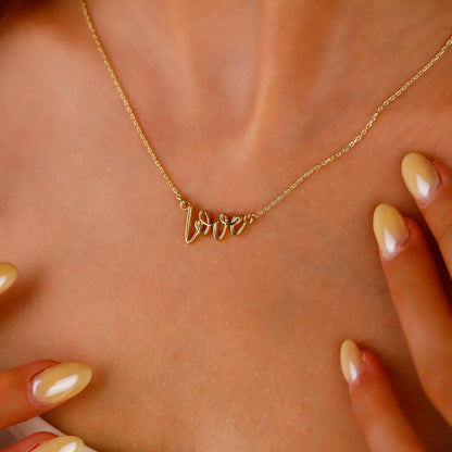 Gold 'love' necklace on a person's neck with a close-up of hands.