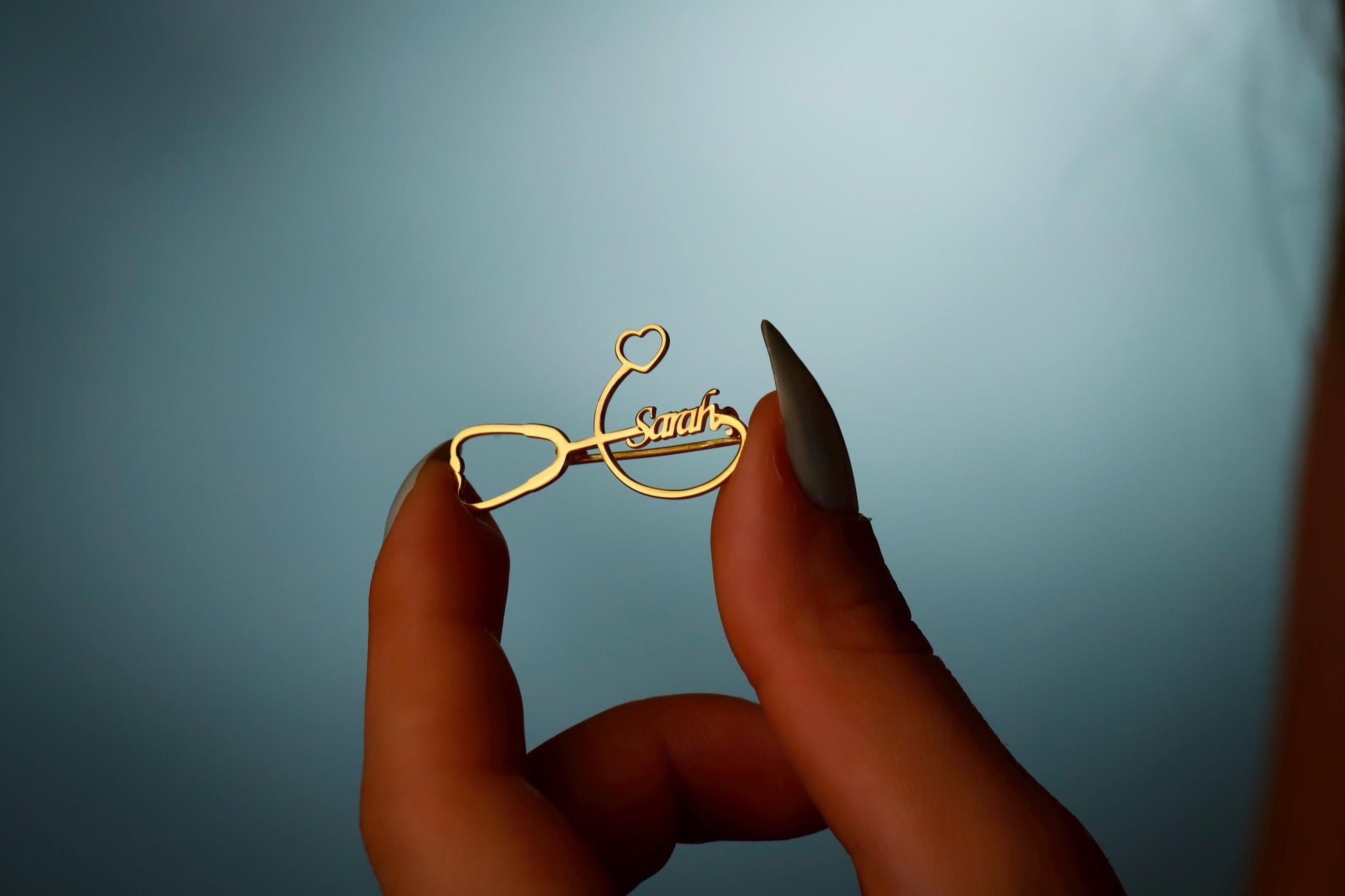 Gold eyeglass frame with 'Swarovski' branding held between fingers against a blue background