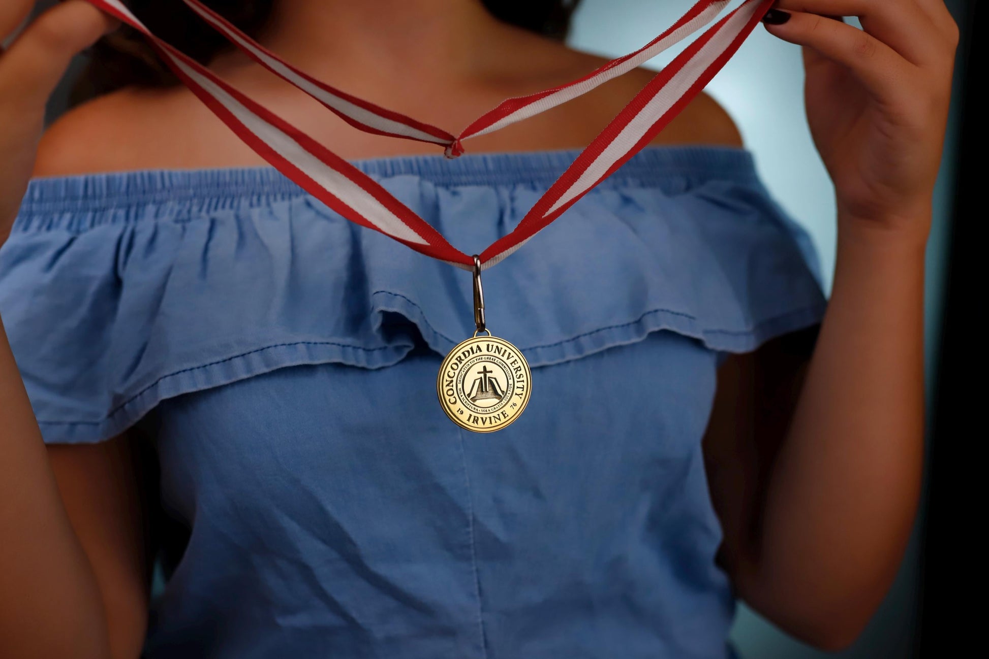 Person wearing a blue off-shoulder top with a gold medal on a red and white ribbon.