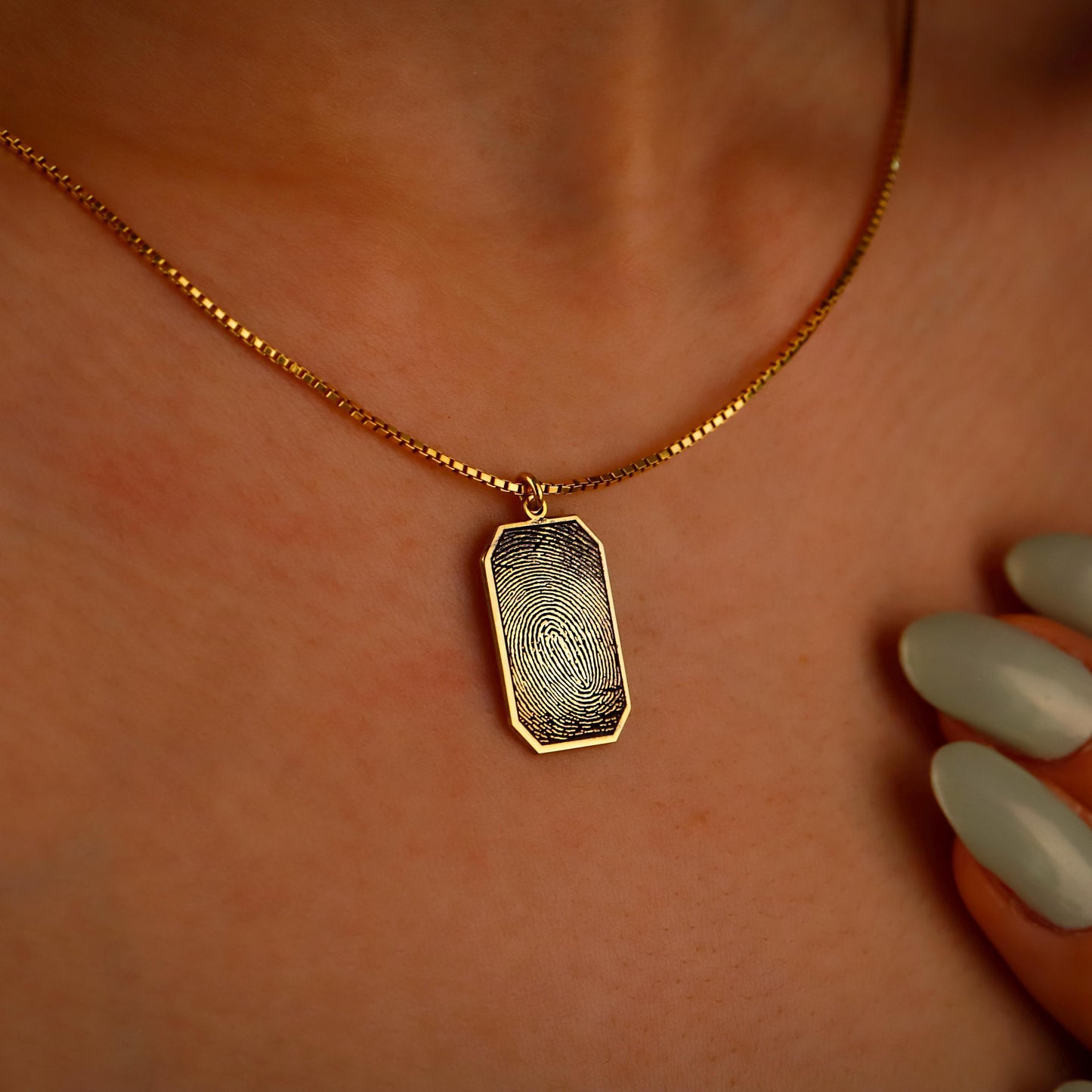 Gold necklace with a fingerprint pendant on a person's neck.