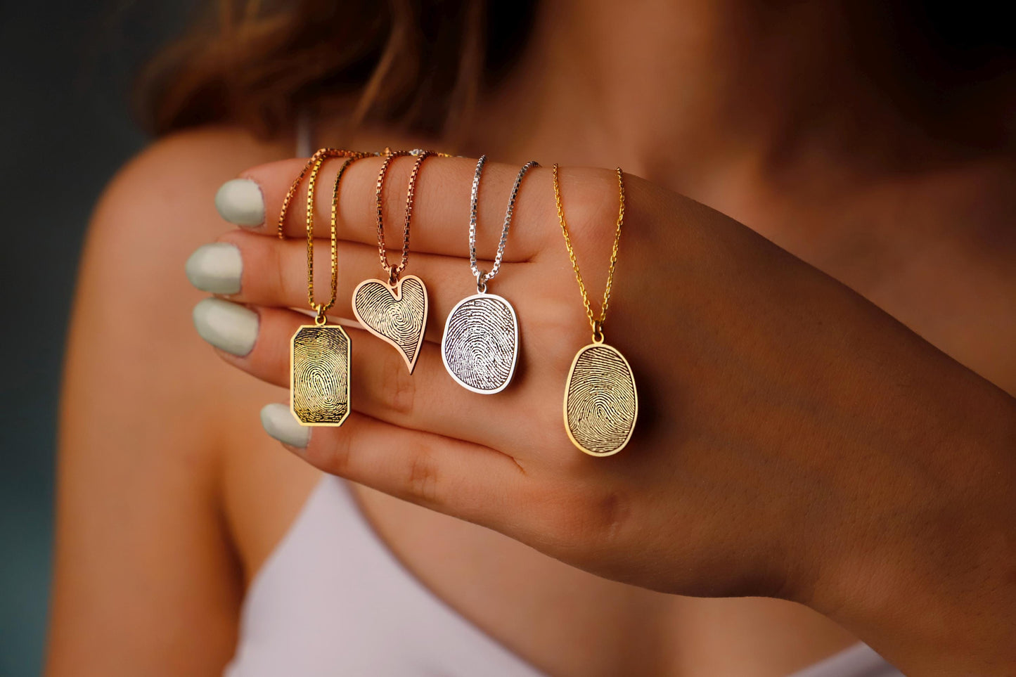Hand holding five gold necklaces with different pendants against a blurred background