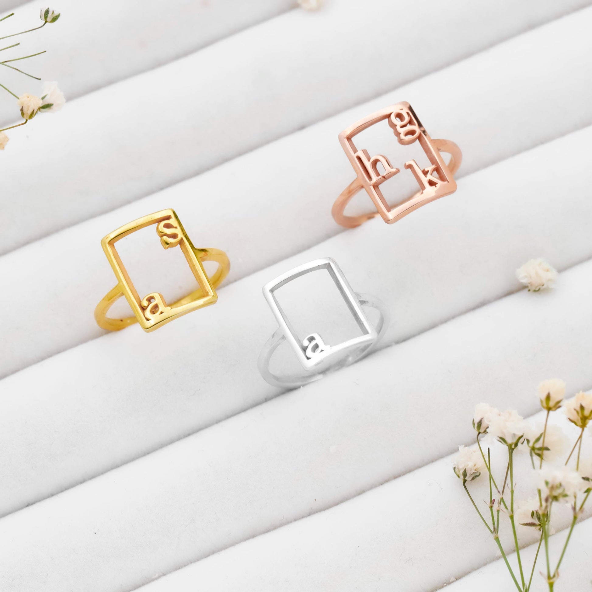 Three rings in gold, silver, and rose gold on a white surface with small flowers.