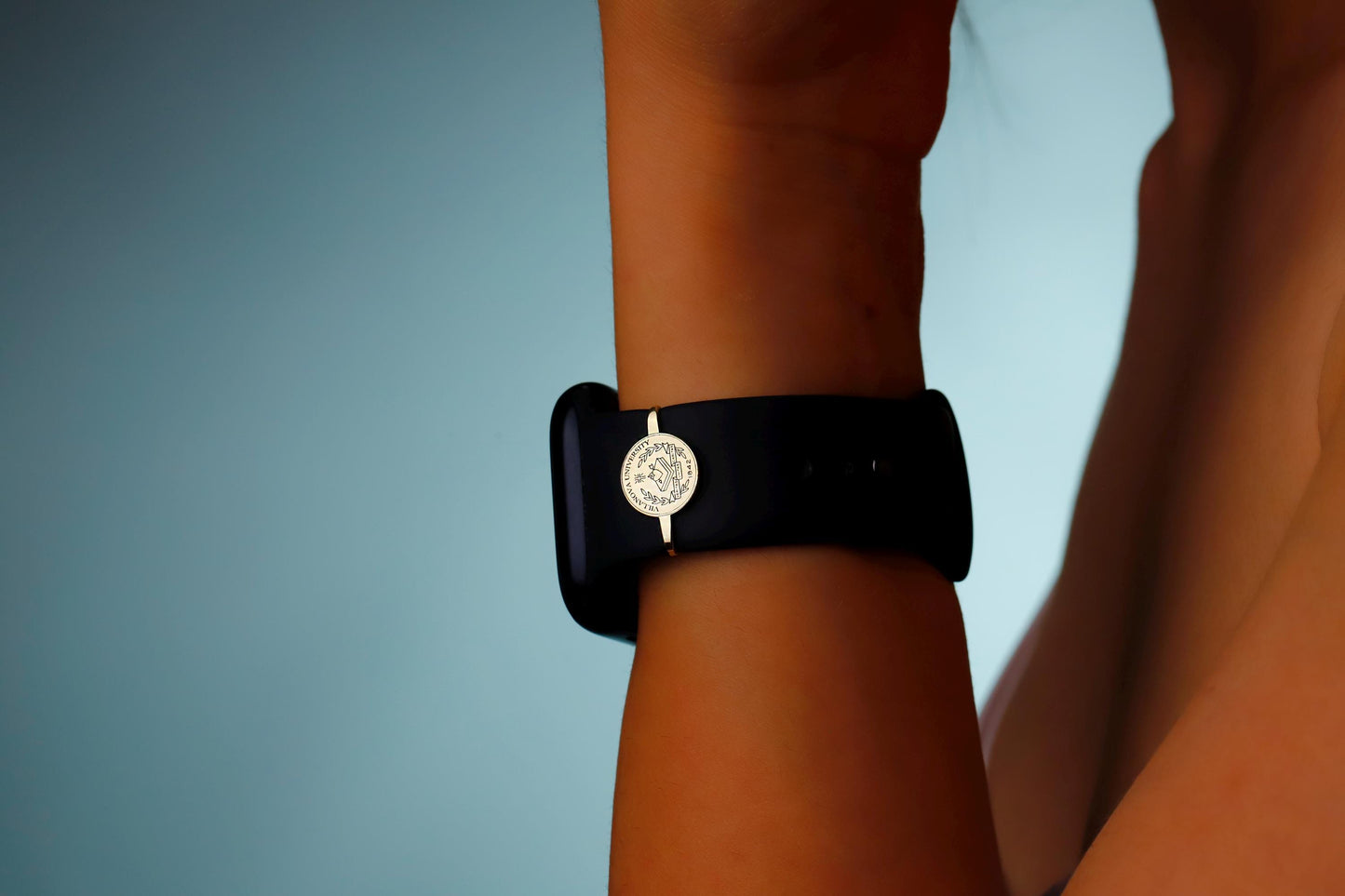 Black wristband with a gold emblem on a person's wrist against a blue background