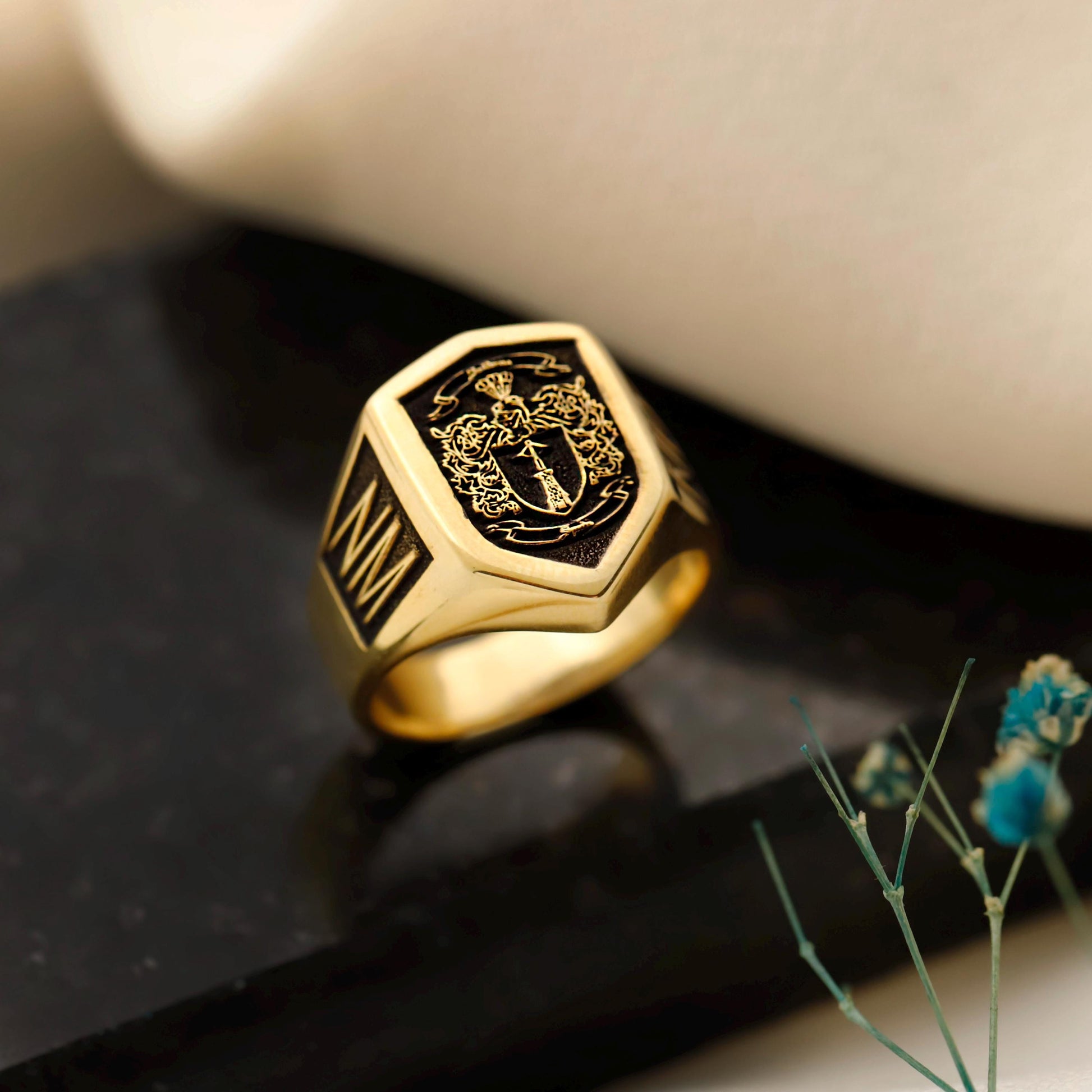 Gold ring with black engraved design on a dark surface with blurred background