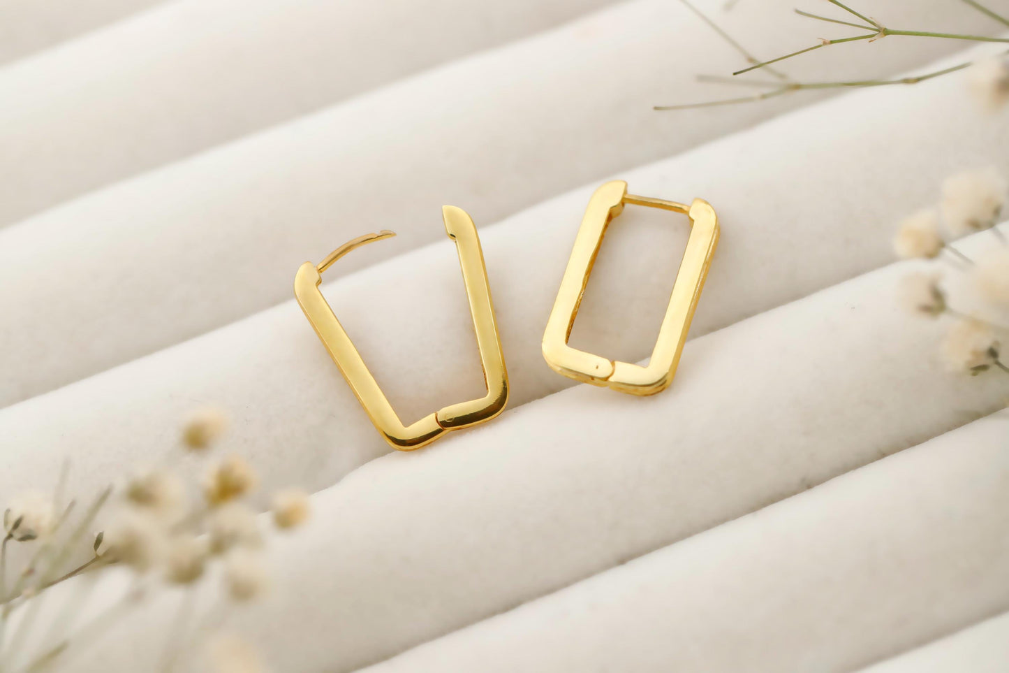 Gold hoop earrings on a soft beige fabric background with dried flowers.