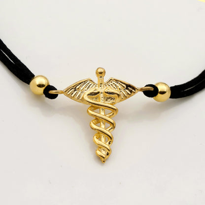 Gold medical symbol pendant on a black cord against a white background