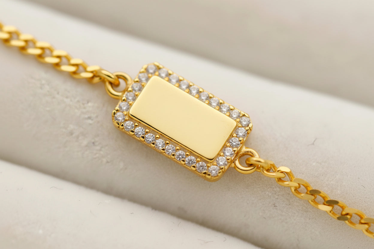 Gold bracelet with a rectangular charm featuring a symbol on a beige surface