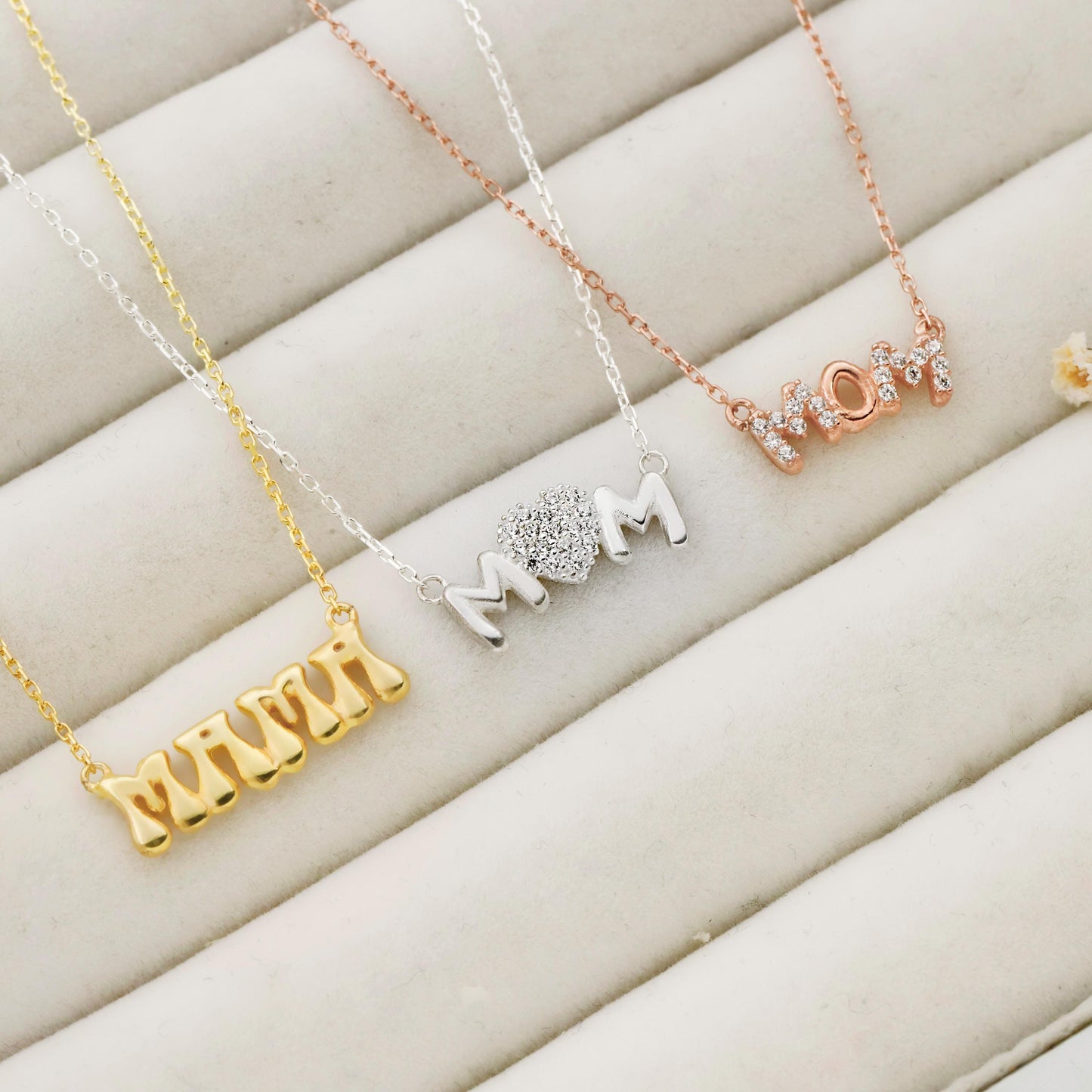 Four necklaces in gold, silver, and rose gold on a beige surface
