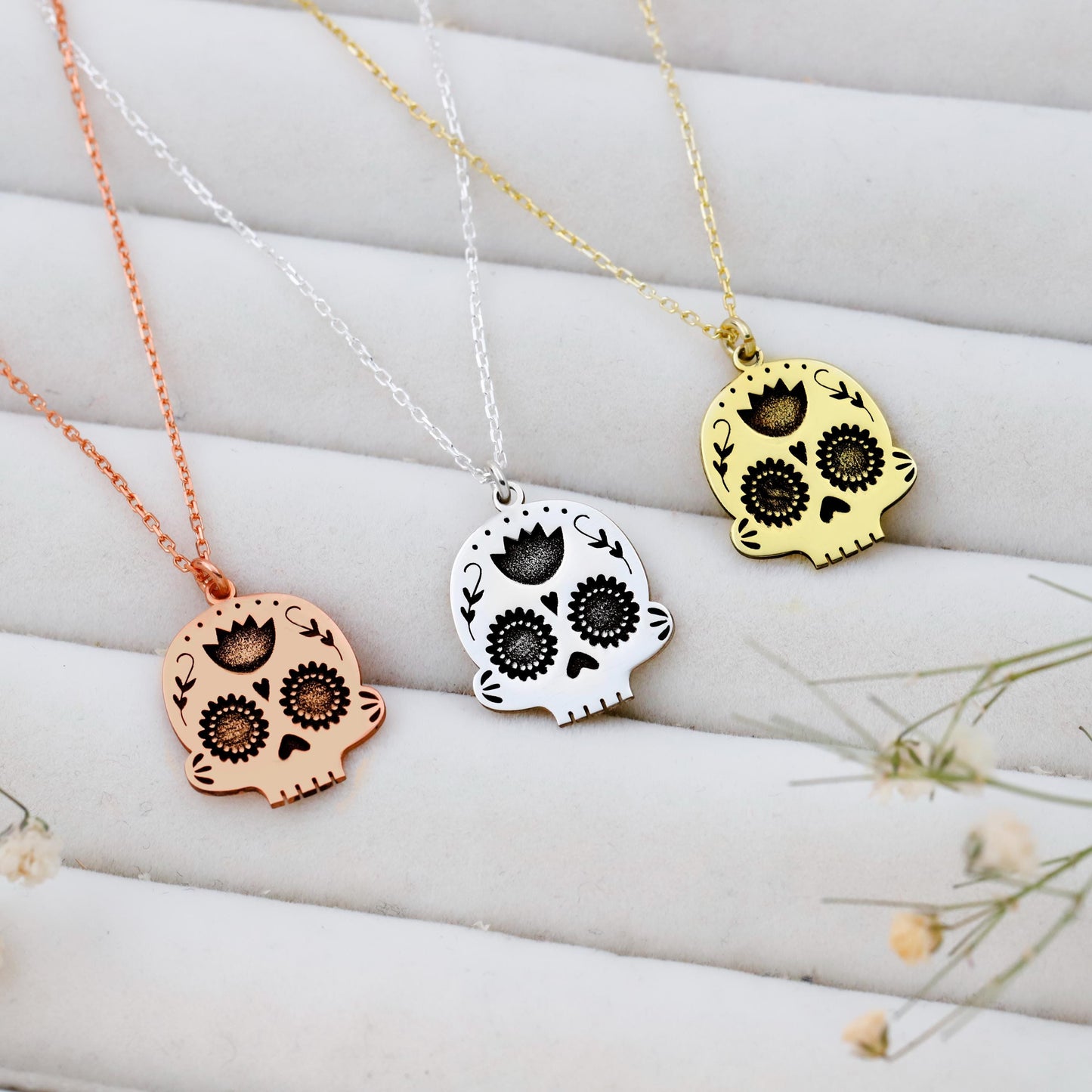 Three skull-shaped pendants on necklaces with rose gold, silver, and gold colors against a white background.