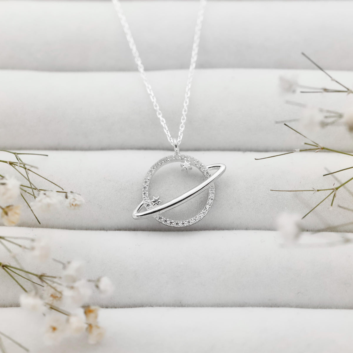 Silver necklace with a circular pendant on a white fabric background with flowers.