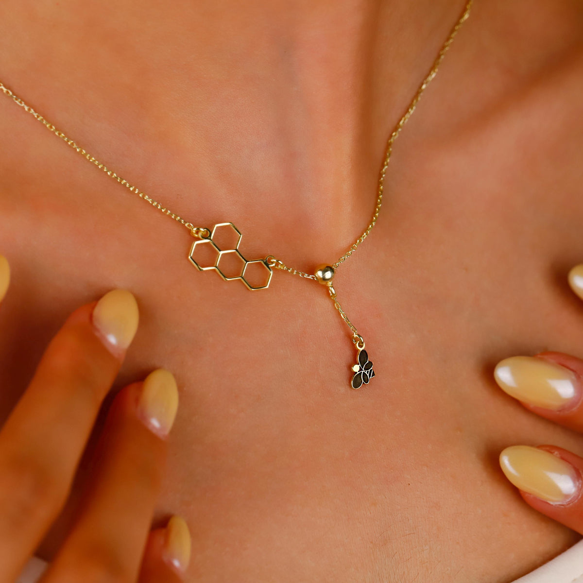 Gold necklace with honeycomb and bee pendant on a person's neck