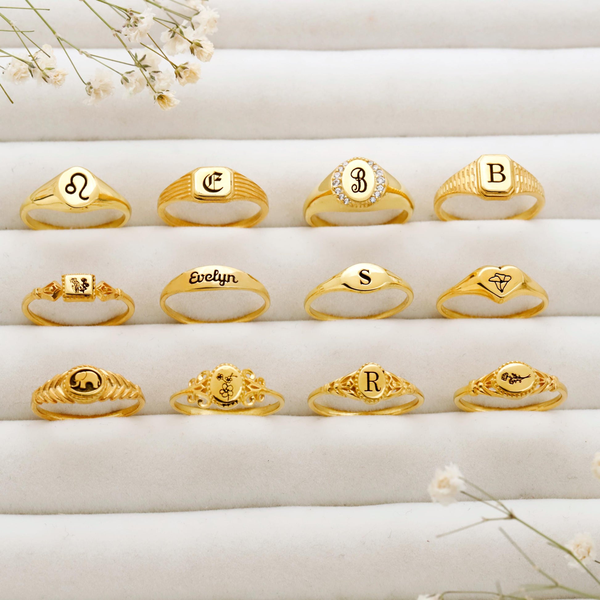 Collection of gold rings with various designs and letters on a white surface.