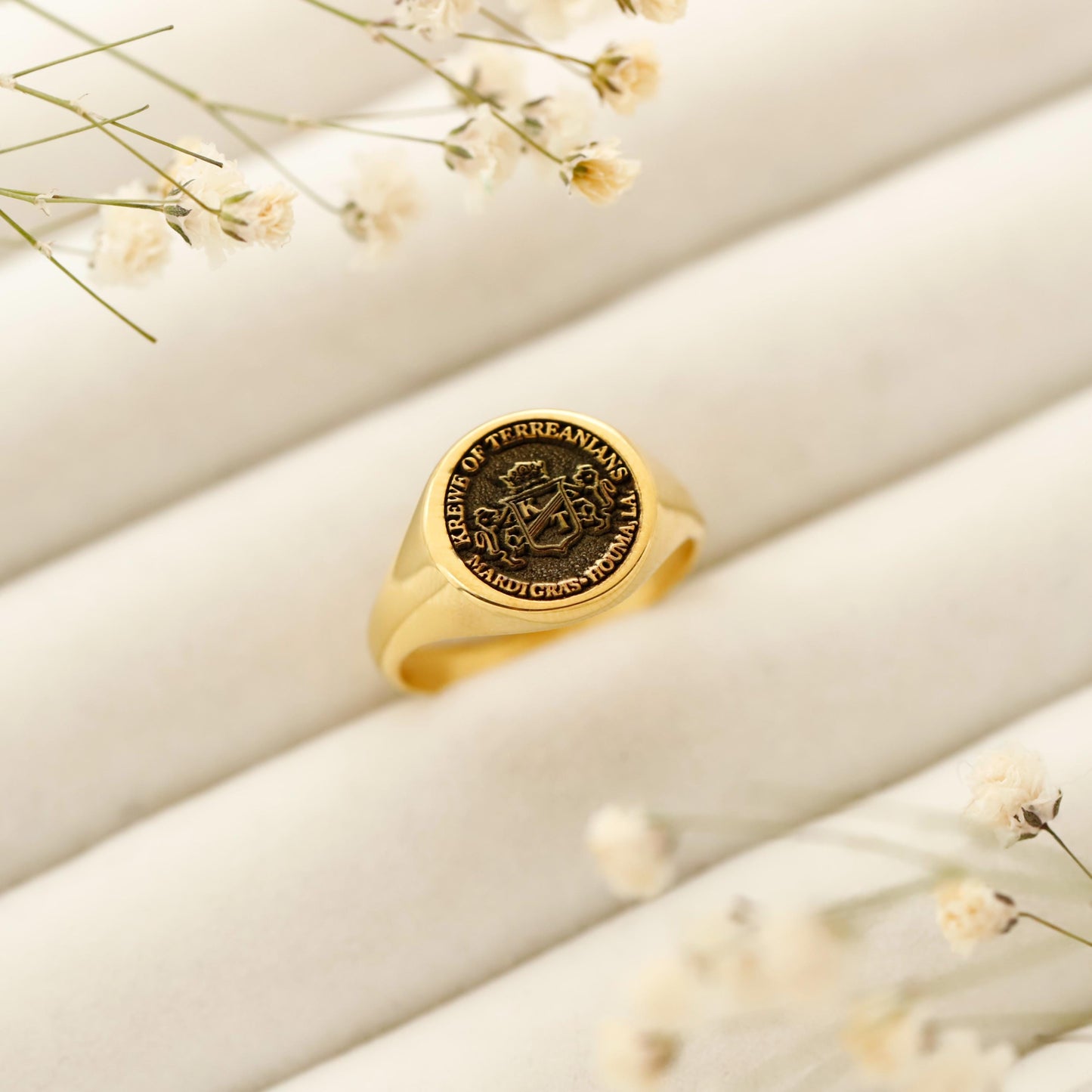Gold ring with engraved design on a beige surface with small flowers