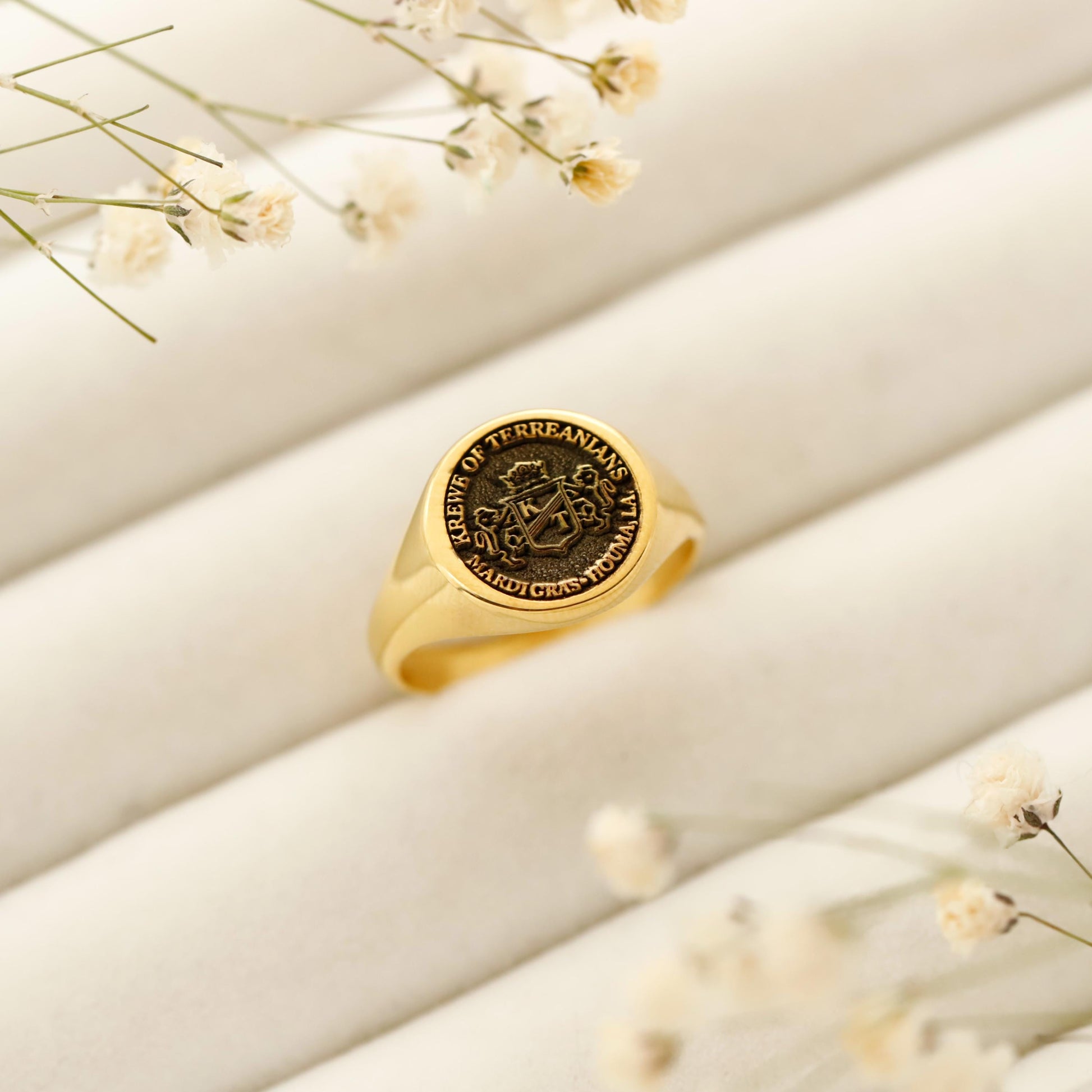 Gold ring with engraved design on a beige surface with small flowers