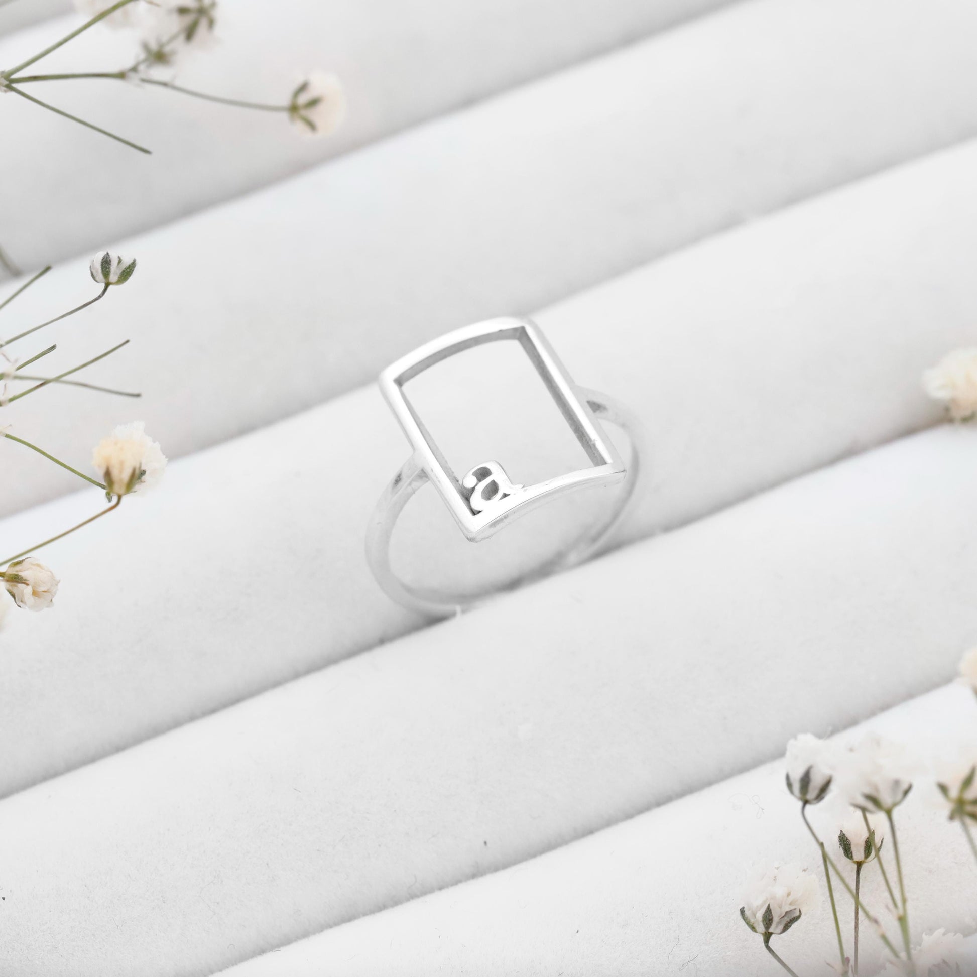 Silver ring with a diamond on a white fabric background with small flowers.