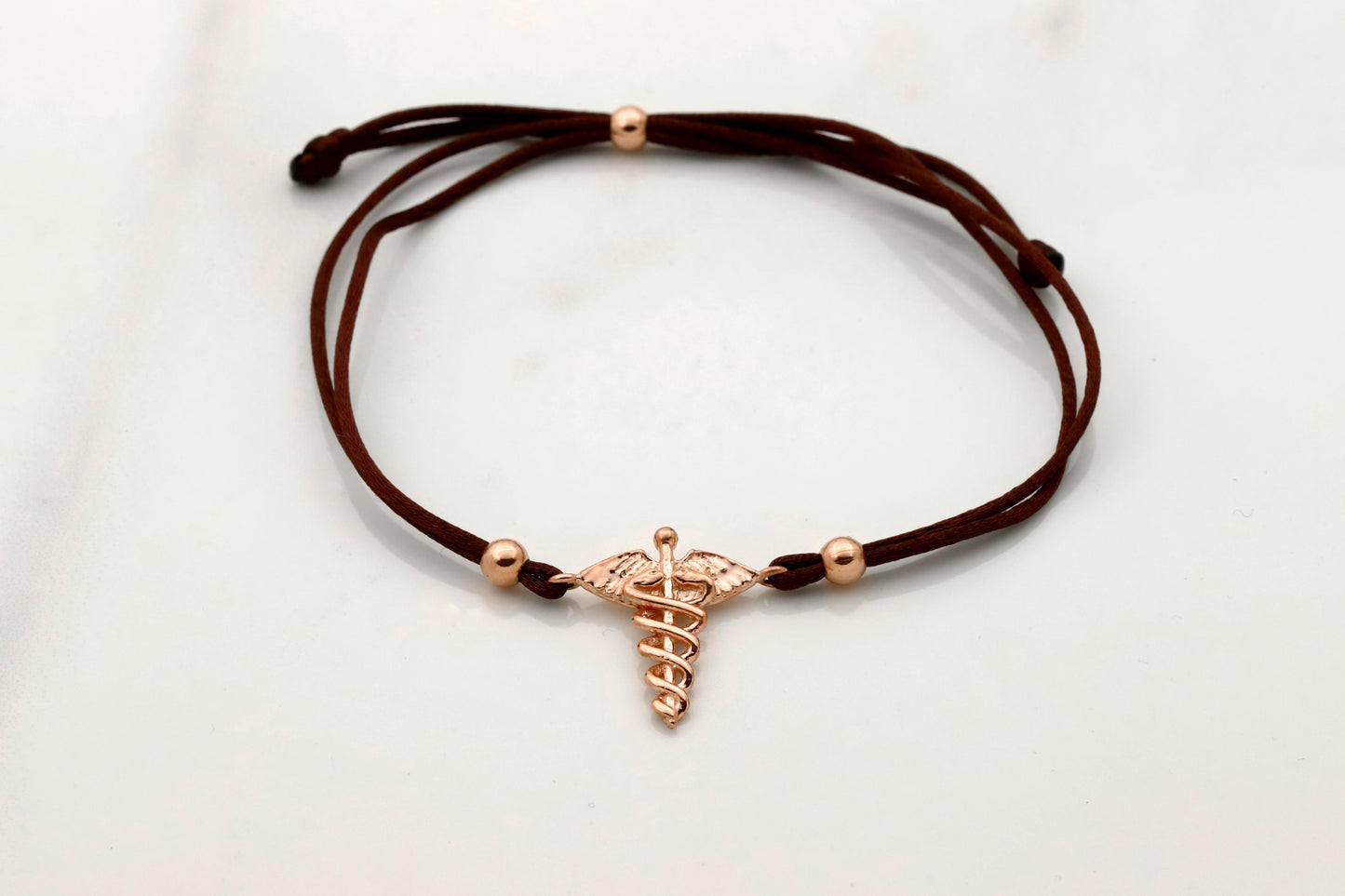 Brown cord bracelet with a rose gold charm on a light gray background