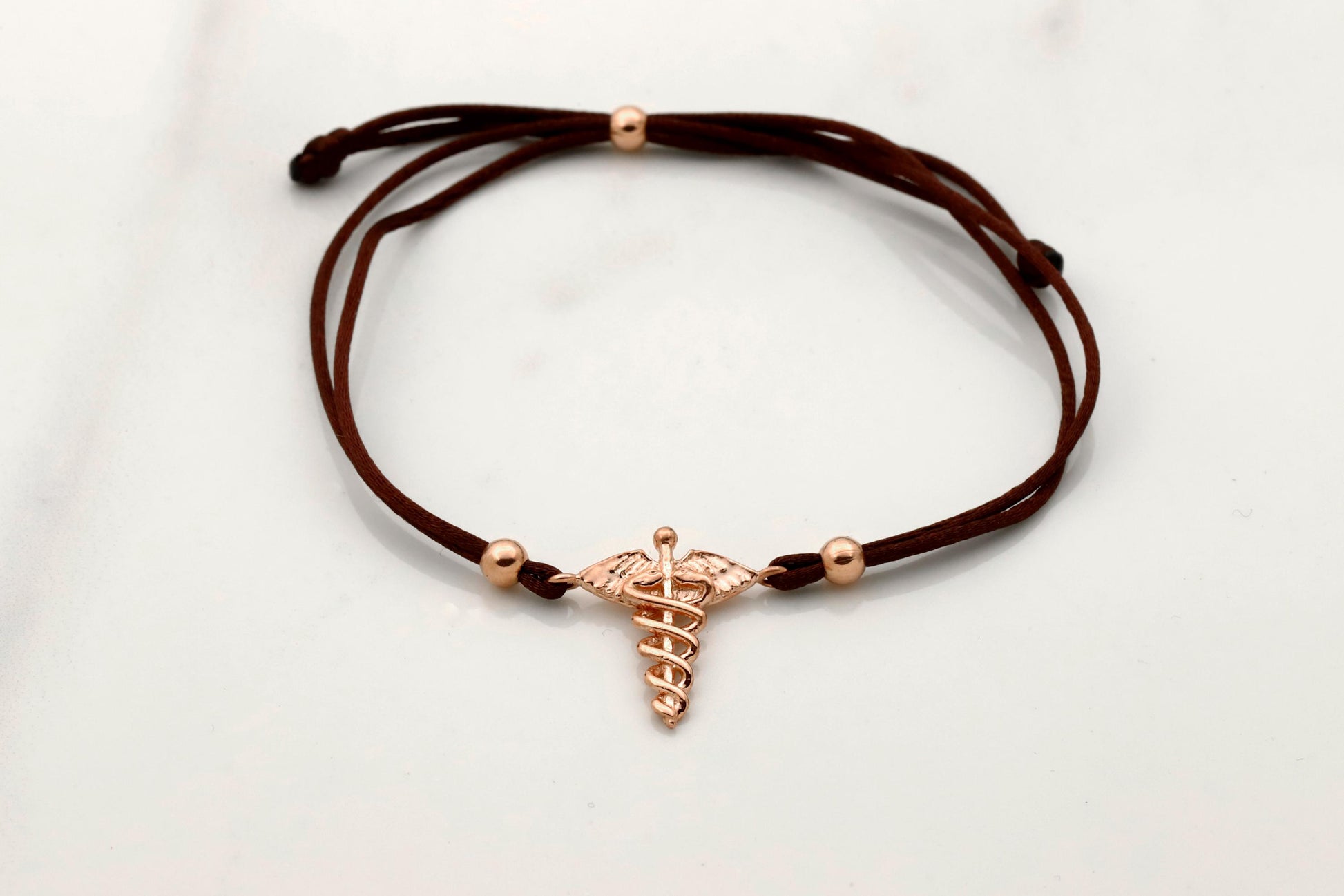 Brown cord bracelet with a rose gold charm on a light gray background