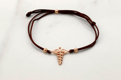 Brown cord bracelet with a rose gold charm on a light gray background