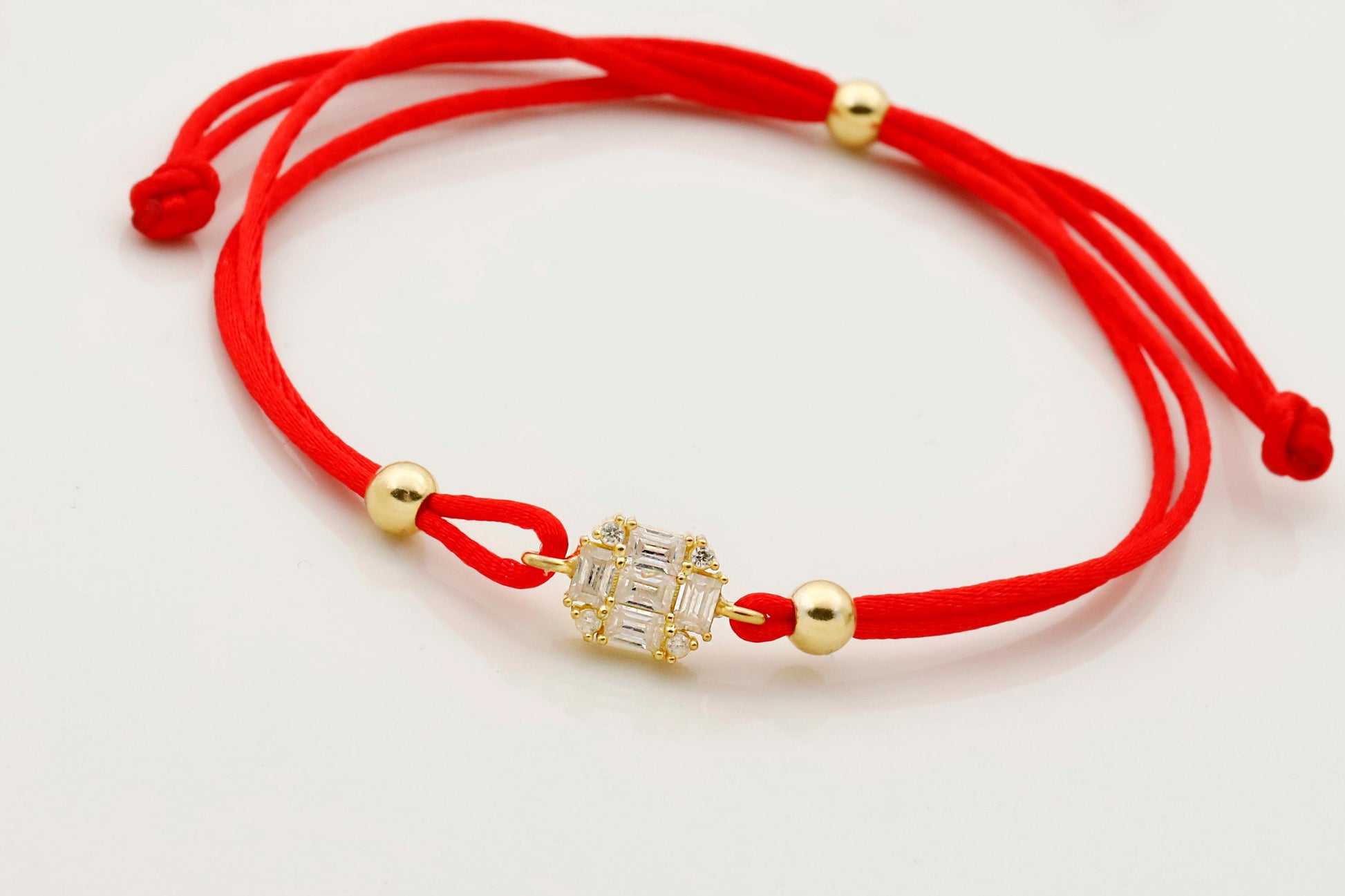 Red string bracelet with gold beads and a decorative clasp on a white background