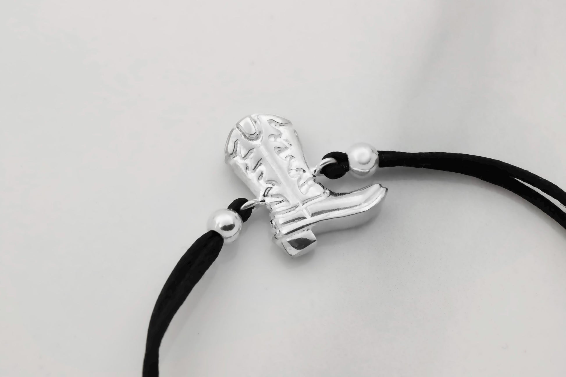 Silver boot charm on a black cord against a light gray background