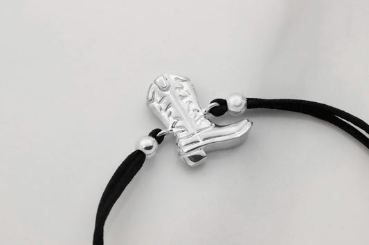 Silver boot charm on a black cord against a light gray background
