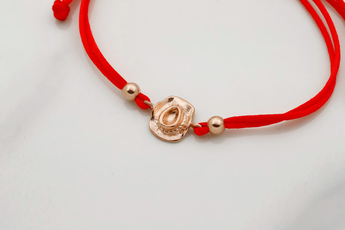 Red bracelet with a gold charm on a light gray background