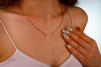Gold necklace with a small pendant on a person wearing a white top.
