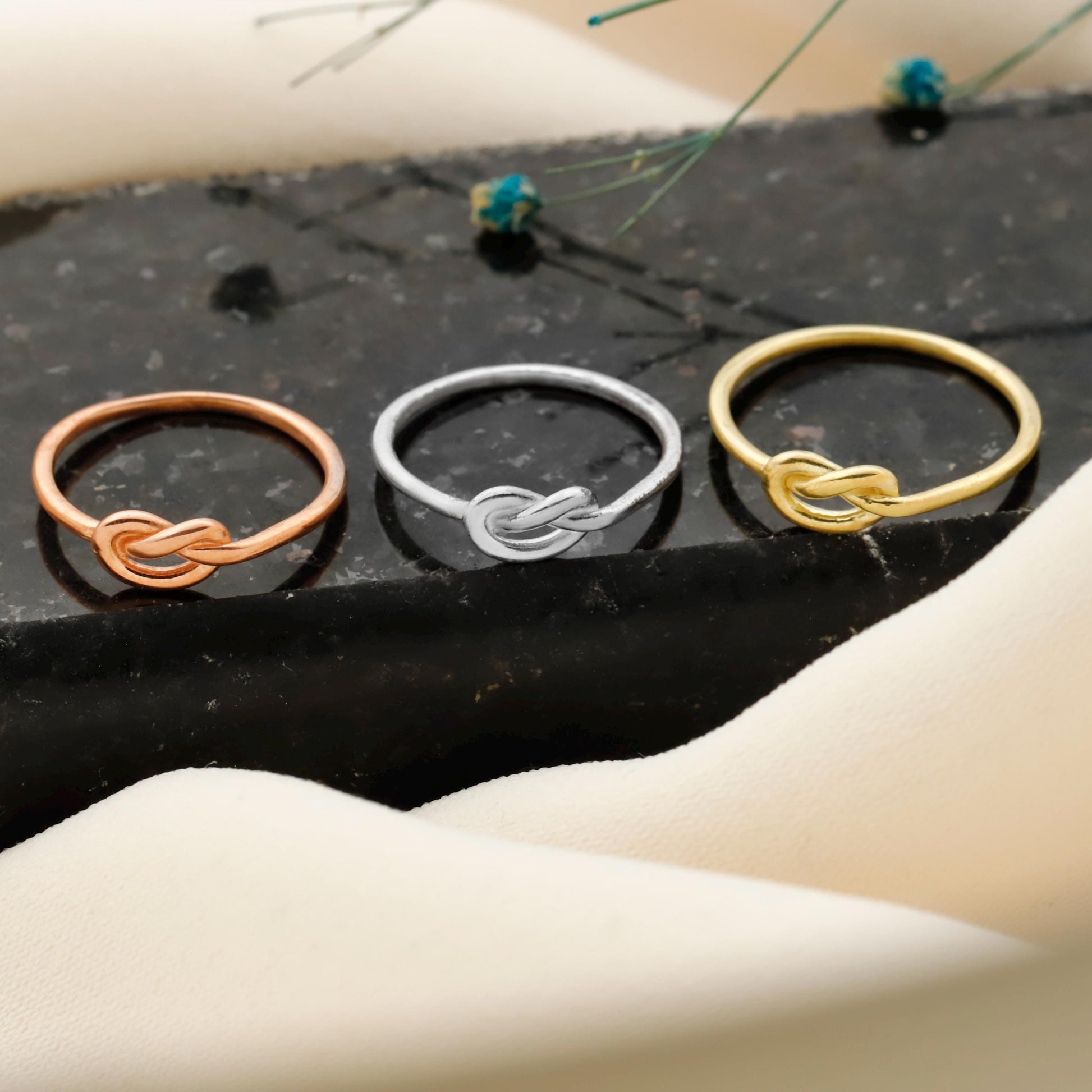 Three knotted rings in bronze, silver, and gold on a dark surface.