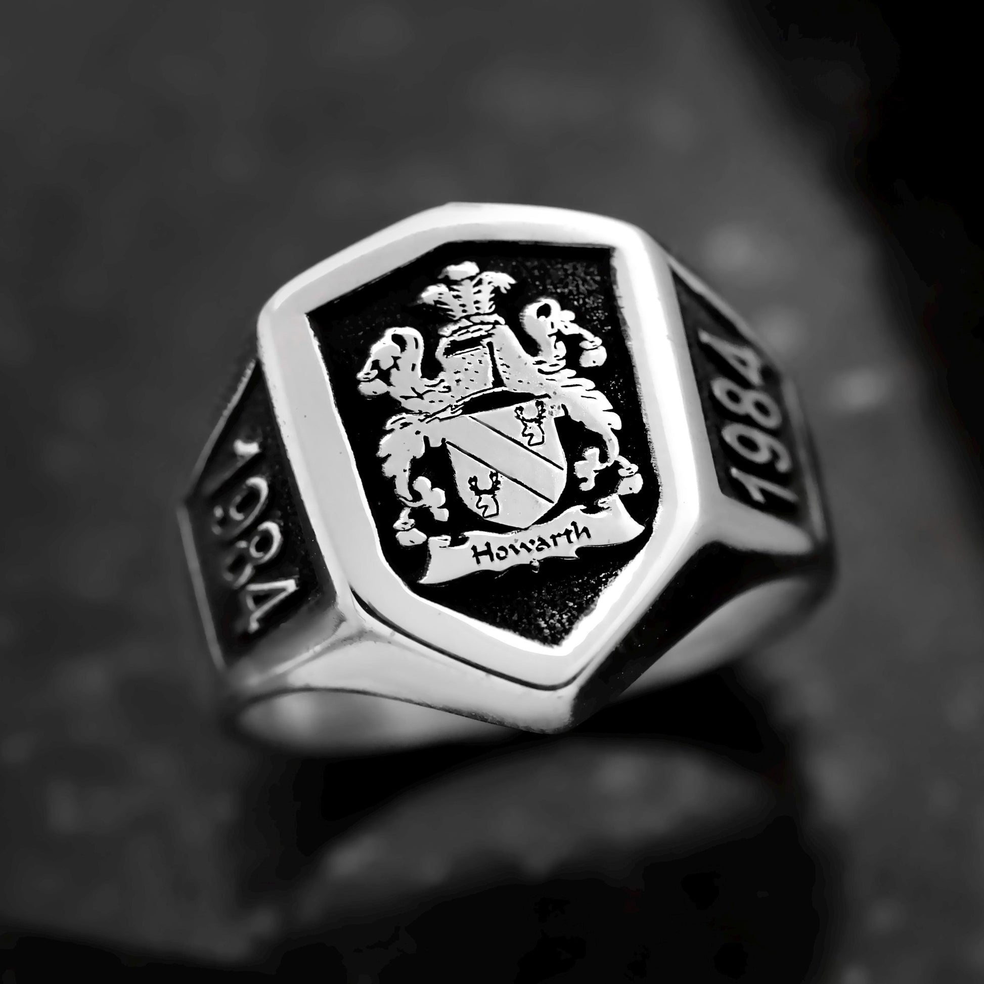 Silver ring with black engraving of a coat of arms and '1984' on a dark background