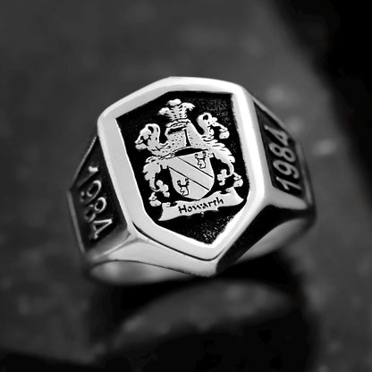 Silver ring with black engraving of a coat of arms and '1984' on a dark background
