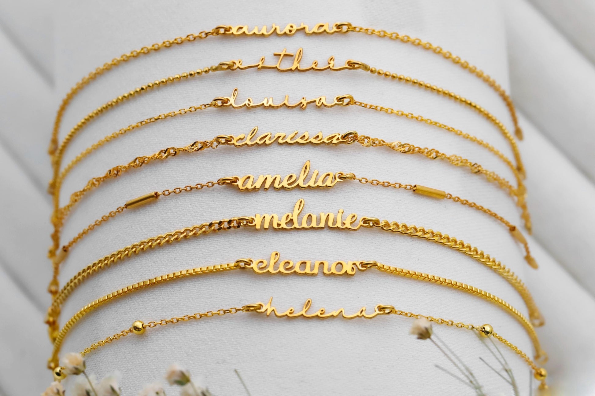 Set of gold name bracelets on a white surface with small flowers.