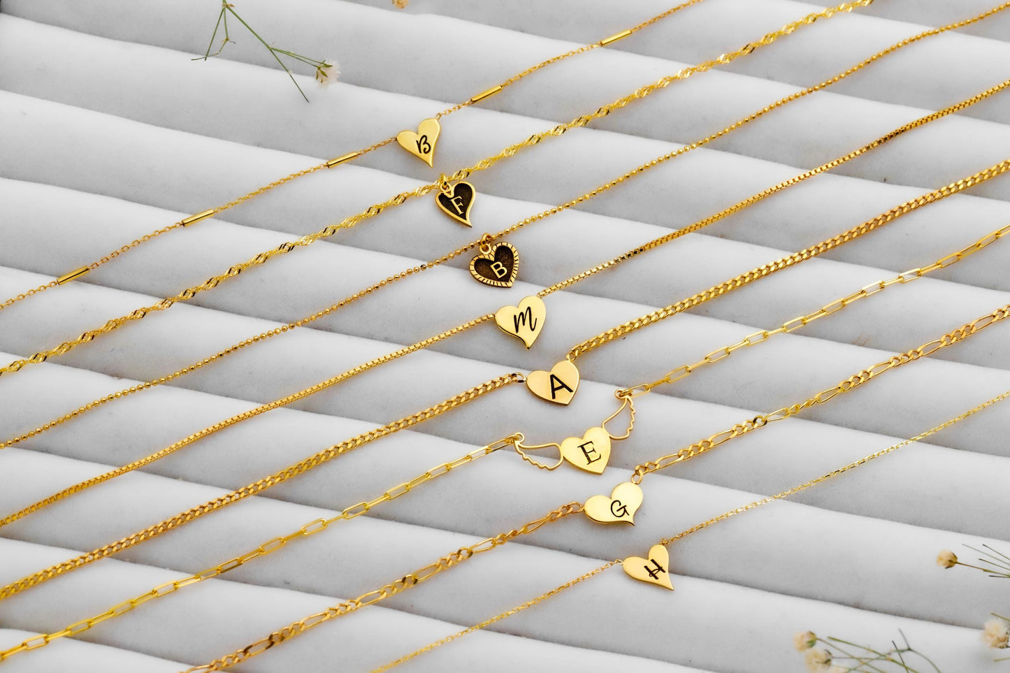 Gold necklaces with heart and letter pendants on a textured white surface