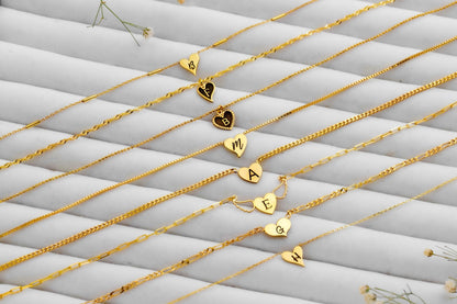 Gold necklaces with heart and letter pendants on a textured white surface