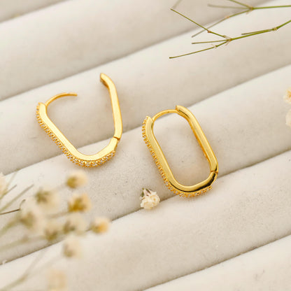 Gold hoop earrings on a soft beige surface with dried flowers.