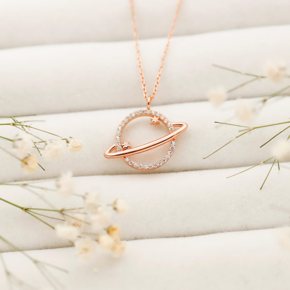 Rose gold necklace with a heart-shaped pendant on a white surface with delicate flowers.