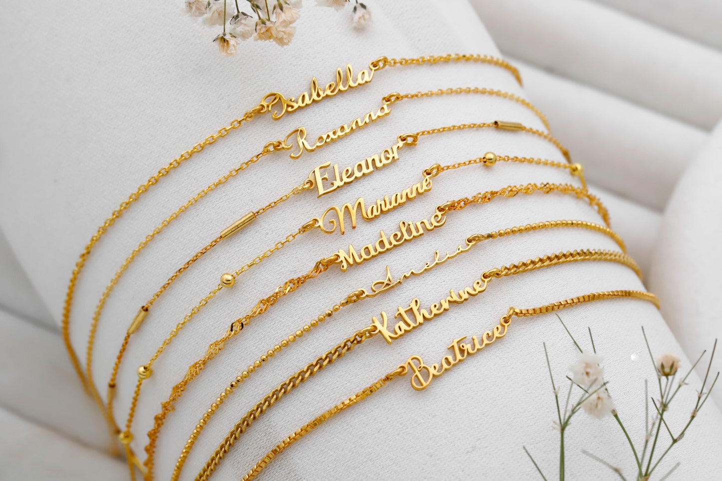 Gold name bracelets on a white surface with floral decorations